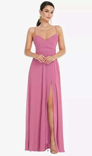 A woman in an Adjustable Strap Wrap Bodice Maxi Bridesmaid Dress by Bergamot Bridal stands gracefully, featuring a front slit that accentuates her poise. Her clasped hands highlight the elegance of the surplice bodice, complemented by gold earrings and heels.