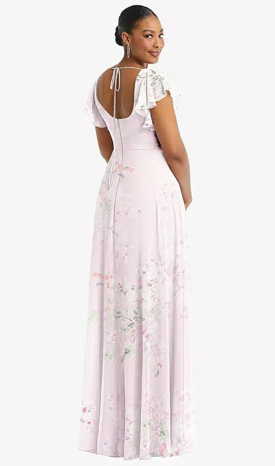 A woman wearing the Bergamot Bridal Flutter Sleeve Scoop Open-Back Chiffon Maxi Bridesmaid Dress - Style 1568 by Dessy, featuring flutter sleeves and a tied back in a light pink floral design, smiles and looks over her shoulder.