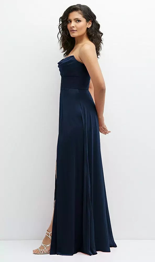 A woman in a navy blue Chiffon Corset Maxi Dress with Removable Off-the-Shoulder Swags by Bergamot Bridal poses sideways against a white background, one leg slightly bent in strappy heels, exuding a high-end aesthetic.