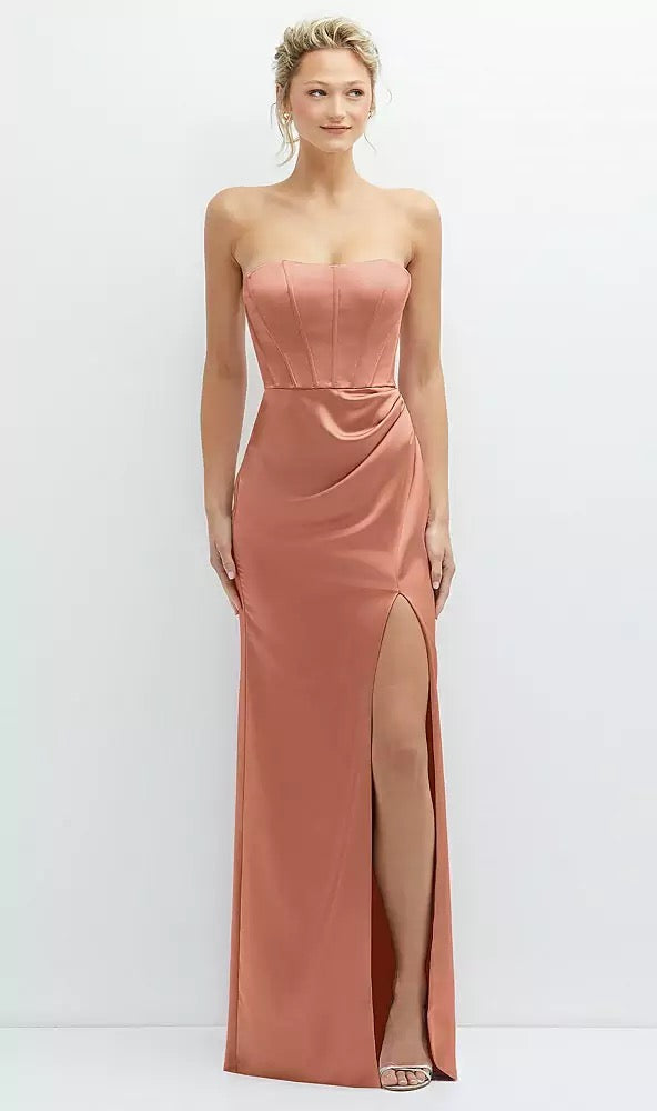 A person stands against a plain background wearing the Strapless Topstitched Corset Satin Maxi Dress with Draped Column Skirt Bridesmaid Dress - Style 6888 by Dessy from Bergamot Bridal, crafted in coral-colored silky-smooth neu stretch charmeuse and featuring a thigh-high slit and corset bodice.