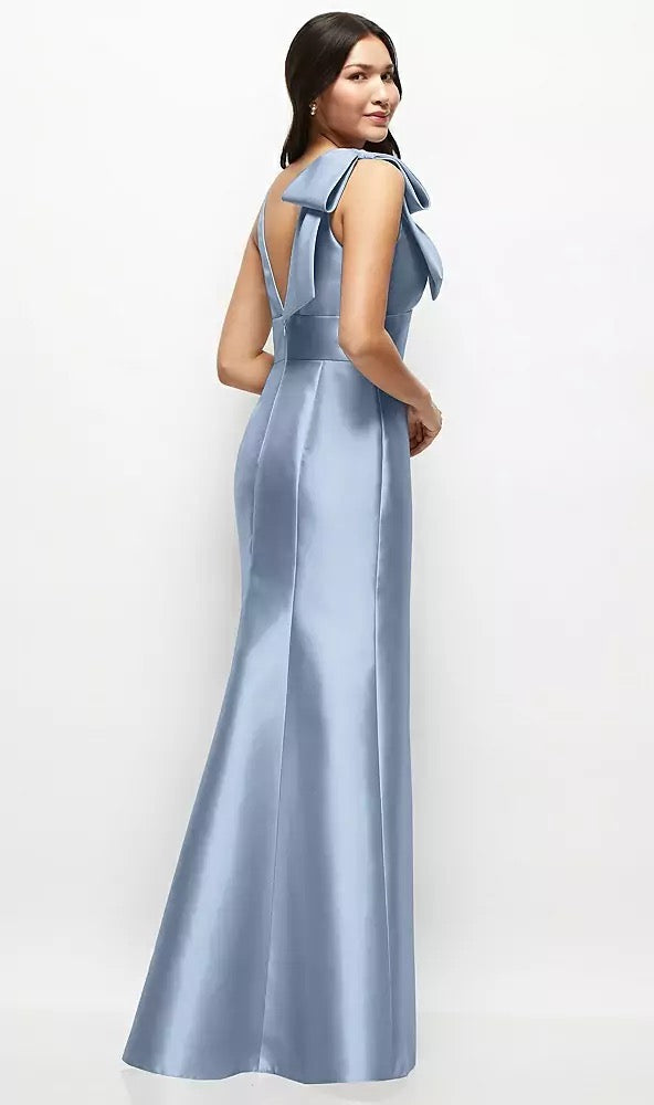 A woman wearing the Bergamot Bridal Deep V-back Satin Trumpet Bridesmaid Dress in a floor-length, light blue design featuring a cascading handcrafted bow at one shoulder, viewed from behind.