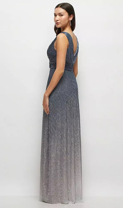 A woman wearing the Bergamot Bridal Draped V-Neck Ombre Pleated Metallic Maxi Bridesmaid Dress - Style 6895OMB by Dessy, is standing sideways against a plain white background, showcasing the shimmering gray fabric and dramatic deep V-back.