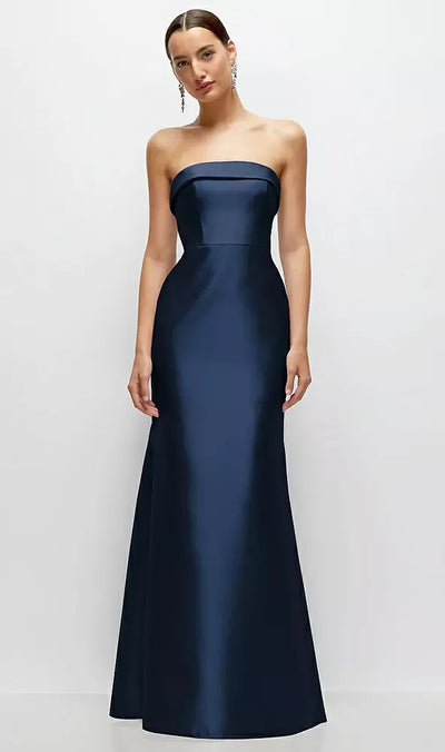 A woman stands against a plain background, facing forward, wearing the Strapless Cuff Neckline Satin Trumpet Bridesmaid Gown by Bergamot Bridal, in navy blue.