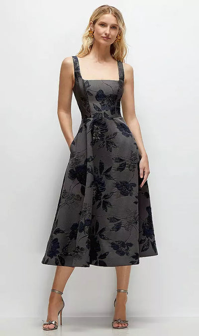 A woman models a Noir Midnight Navy Square Neck Floral Metallic Jacquard Midi Bridesmaid Dress by Bergamot Bridal against a plain background, elegantly paired with metallic high-heeled sandals.