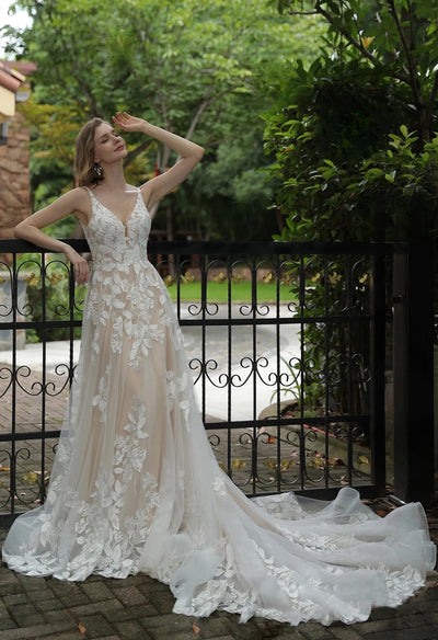 A woman is posing in a Luxurious Floral Lace A-Line Wedding Dress With Sheer Train from Bergamot Bridal in front of a fence at bridal shops london.