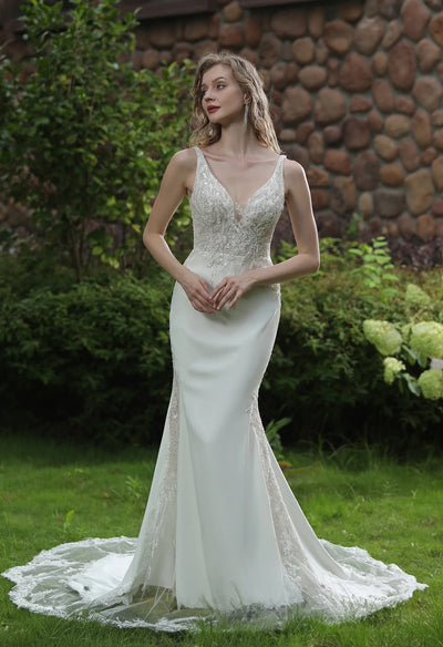 A woman in a Bergamot Bridal Simple Beaded Fit And Flare Gown with V Neckline And Crepe Skirt posing in a garden setting.