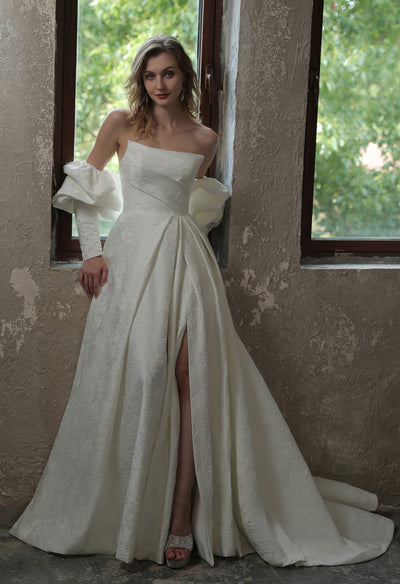 A woman in a white wedding dress leaning against a window at Bergamot Bridal shop wearing the Modern Scoop Neckline Brocade Satin Ball gown.
