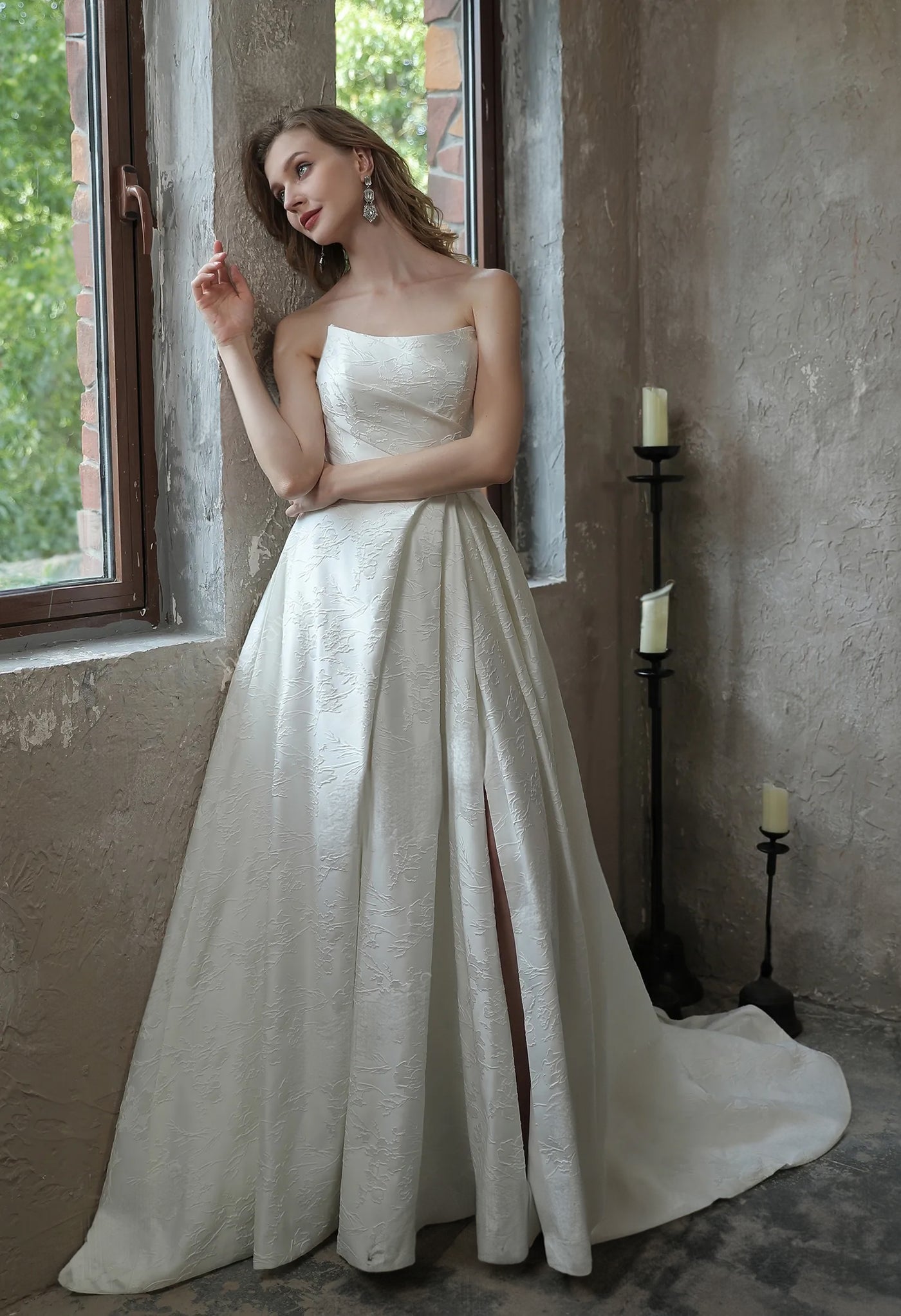 A woman in a white wedding dress leaning against a window at Bergamot Bridal's bridal shop in London, wearing the Modern Scoop Neckline Brocade Satin Ball gown.