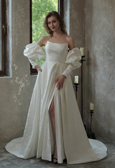 A woman in a white wedding dress is posing in front of a window at Bergamot Bridal, wearing the Modern Scoop Neckline Brocade Satin Ball gown.