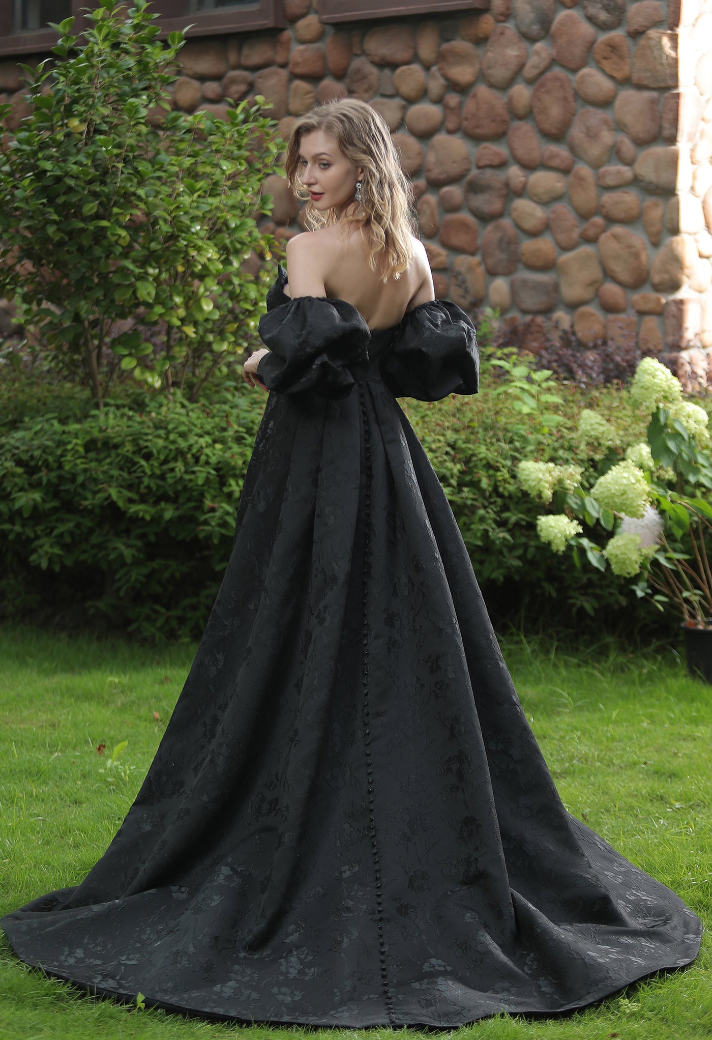 A woman in a black dress standing in the Bergamot Bridal garden, wearing the Modern Scoop Neckline Brocade Satin Ball gown.