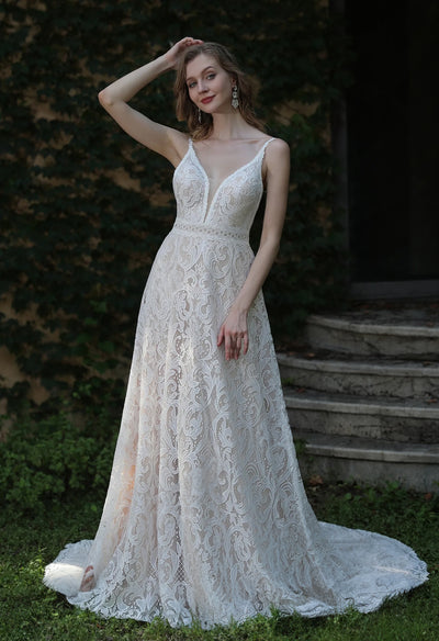 A white boho lace wedding dress with spaghetti straps and removable bell sleeves, posing in front of a garden for Bergamot Bridal bridal shops London.