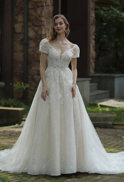A woman in a Sparkly Ball Gown Wedding Dress With Beaded Spaghetti Straps and Detachable Sleeves from Bergamot Bridal, standing in front of a brick wall.