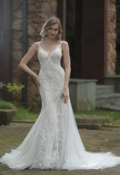 A woman in an elegant Bergamot Bridal Classic V-Neck Allover Lace Fit And Flare Wedding Dress with a train posing outdoors.
