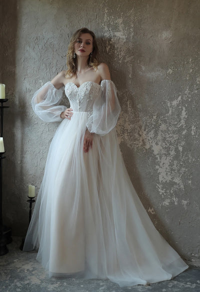 A bride in an Enchanting Pleated Tulle A-line Bergamot Bridal wedding dress with puff sleeves leaning against a wall.