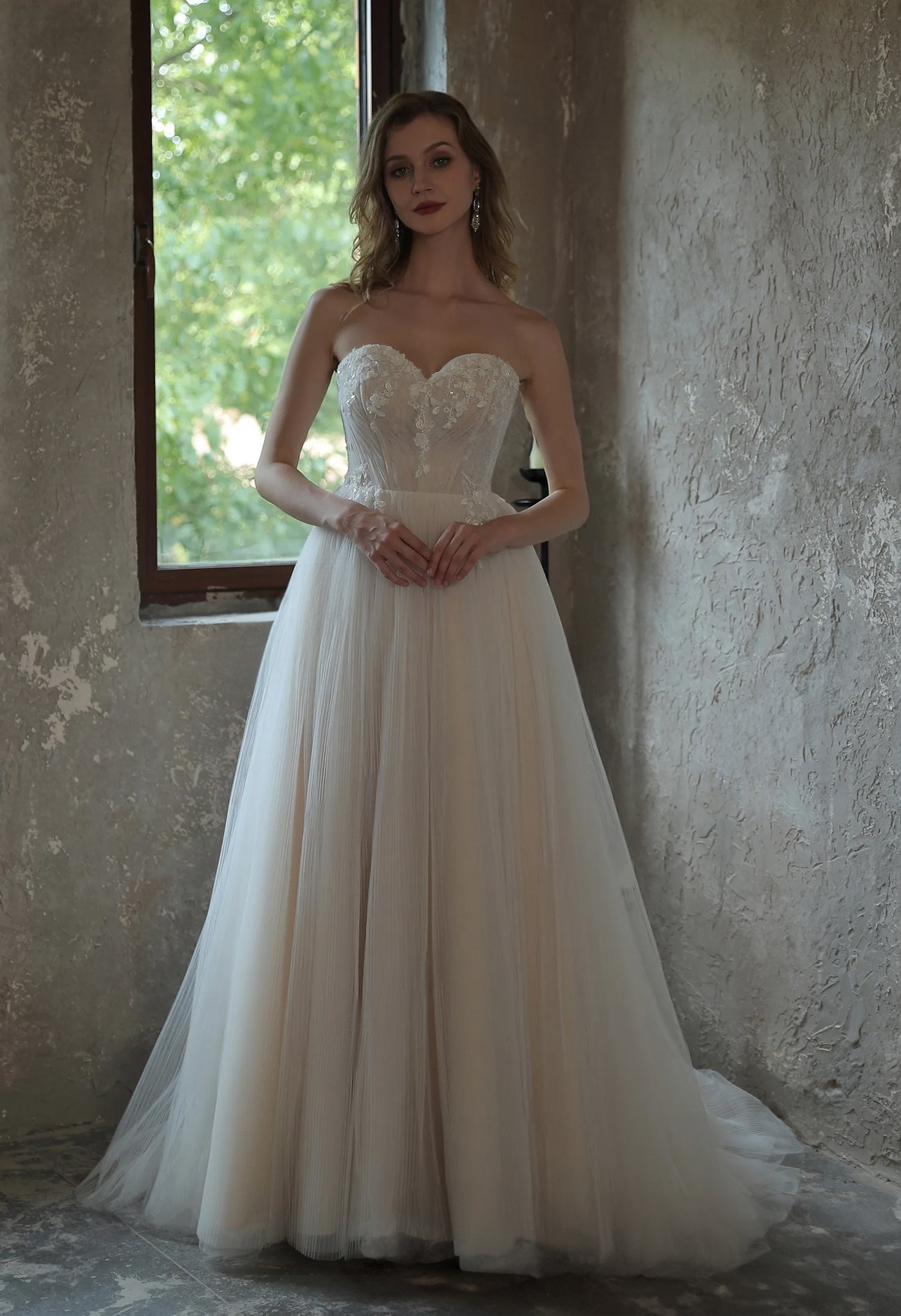 An Enchanting Pleated Tulle A-line Wedding Dress With Puff Sleeves by Bergamot Bridal in a bridal shop in London standing in an empty room.
