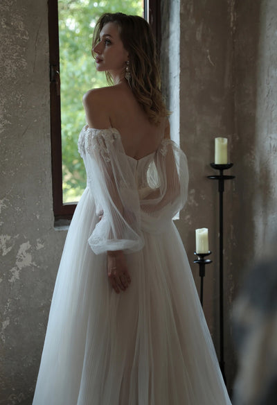 An Enchanting Pleated Tulle A-line Wedding Dress With Puff Sleeves by Bergamot Bridal is standing in front of a window at a bridal shop in London.