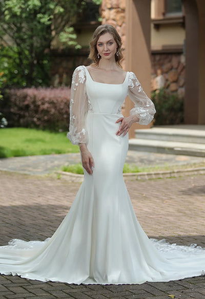 Woman in an elegant Bergamot Bridal Square Neck Crepe Fit And Flare Wedding Dress With Tulle Bishop Sleeves, posing outdoors.