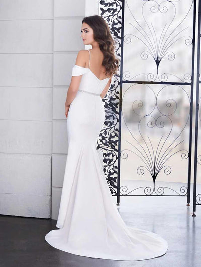 A woman in a white off-the-shoulder bridal gown with a beaded belt, standing by a decorative metal gate, looking over her shoulder wearing the Bergamot Bridal Paloma Blanca 4854 Simple Fit and Flare Gown - Off The Rack.