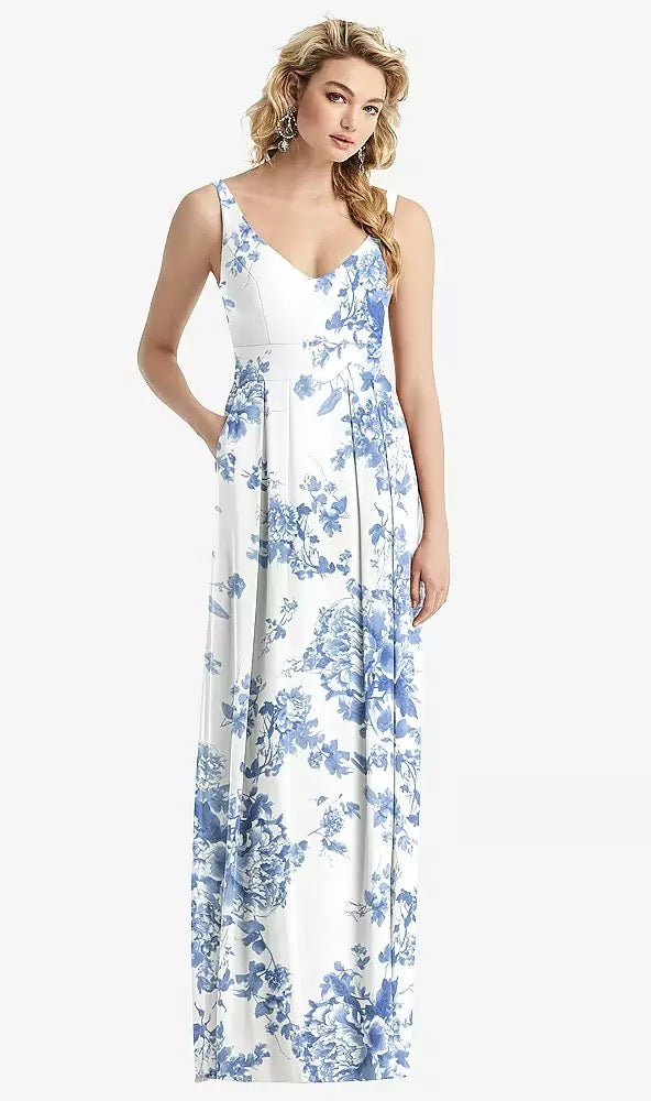 A woman wearing the Bergamot Bridal Sleeveless Pleated Skirt Maxi Bridesmaid Dress with Pockets in style 1519, featuring a white and blue floral pattern and V-neck design, stands gracefully against a plain background, perfect for any special occasion.