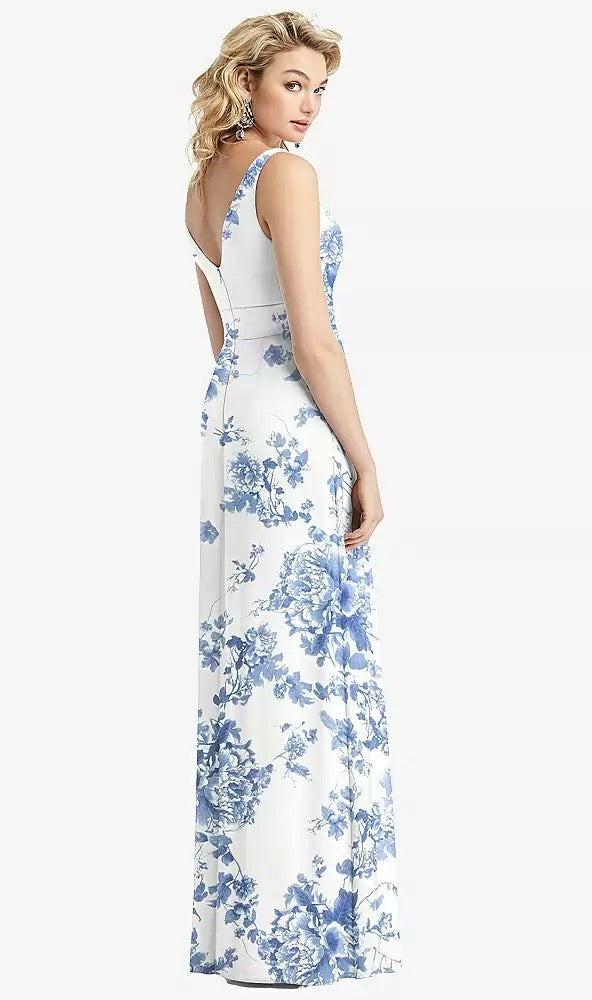 A woman elegantly poses in the Sleeveless Pleated Skirt Maxi Bridesmaid Dress with Pockets, Style 1519 by Bergamot Bridal, featuring exquisite blue floral patterns, making it ideal for any special occasion.