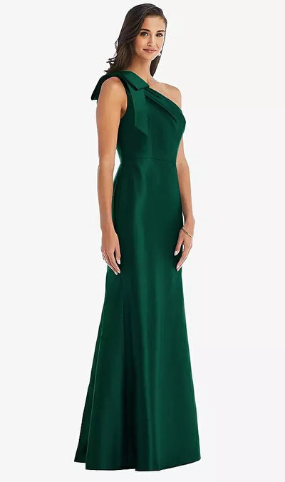 A person wearing a long, dark green Bow One-Shoulder Satin Trumpet Gown Bridesmaid Dress by Bergamot Bridal, standing against a plain background.