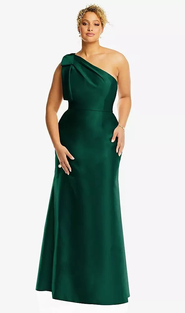 A person stands gracefully against a plain background, elegantly adorned in the Bow One-Shoulder Satin Trumpet Gown Bridesmaid Dress (Style D794 by Dessy) from Bergamot Bridal.