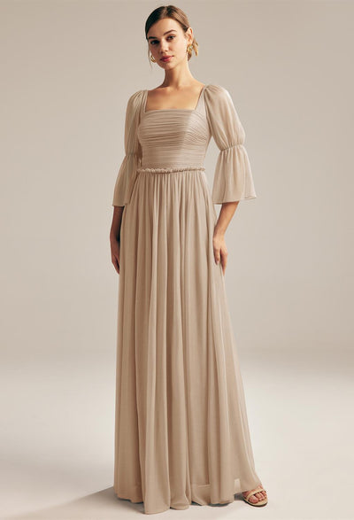 A woman in an elegant beige Liza - Glitter Mesh Bridesmaid Dress with puff sleeves and gathered waist, posing confidently against a light background from Bergamot Bridal.