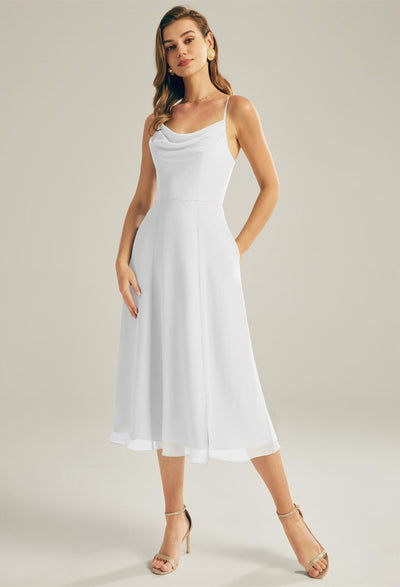 A woman confidently poses in a Bergamot Bridal "Maribel" chiffon bridesmaid dress, featuring a white sleeveless midi design and practical pockets—a perfect choice for those looking for affordable wedding or elegant bridesmaid dresses at a bridal shop in London, Ontario.