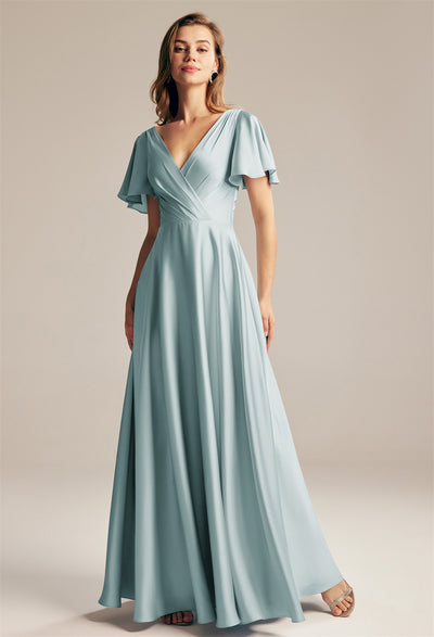 A woman wearing the Furst Satin Charmeuse Bridesmaid Dress by Bergamot Bridal, in a light blue hue with short, flowing sleeves, stands poised as if she's set for a visit to a bridal shop in London, Ontario.