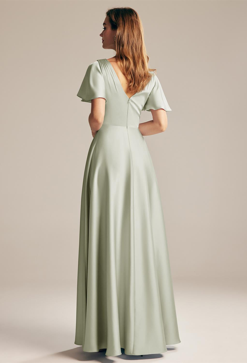 The back view of a woman wearing a Furst - Satin Charmeuse Bridesmaid Dress - Off The Rack in sage green by Bergamot Bridal.