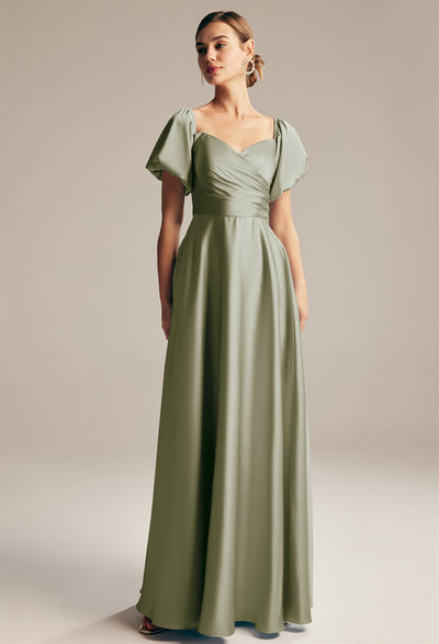 A woman wearing Bergamot Bridal's "Dey - Satin Charmeuse Bridesmaid Dress - Off The Rack" in a light green color stands elegantly against a neutral background, capturing the chic allure of bridesmaid dresses from a stylish bridal shop in London, Ontario.