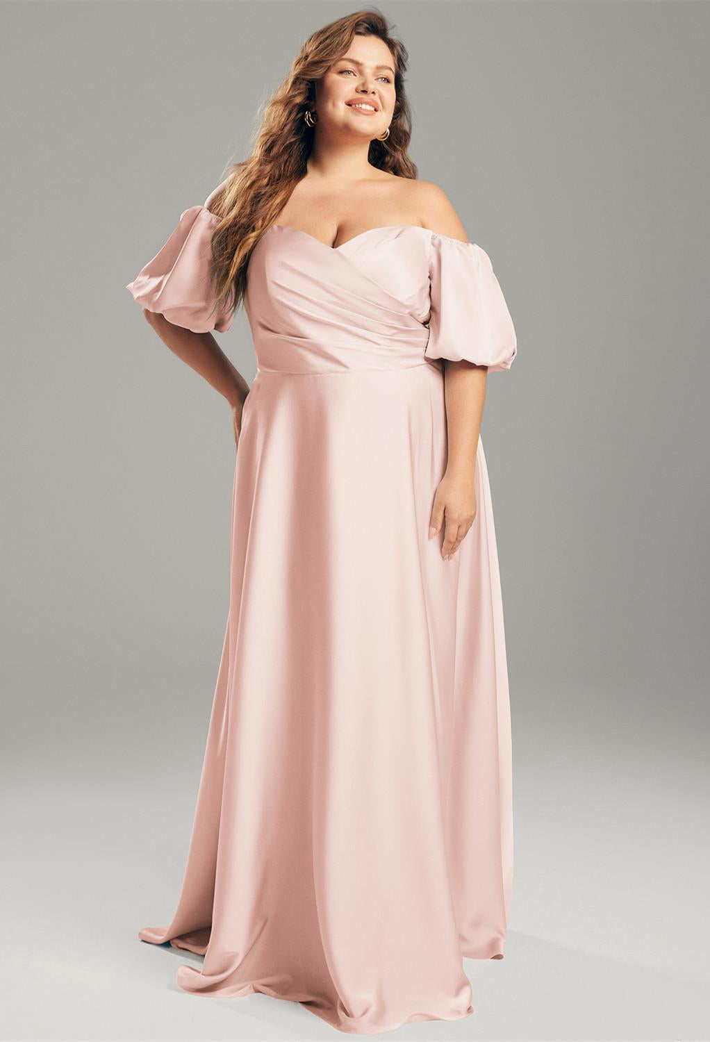 Dressed in the Dey Satin Charmeuse Bridesmaid Dress by Bergamot Bridal, someone stands gracefully against a neutral backdrop, evoking the sophisticated designs typical of a bridal shop in London, Ontario.