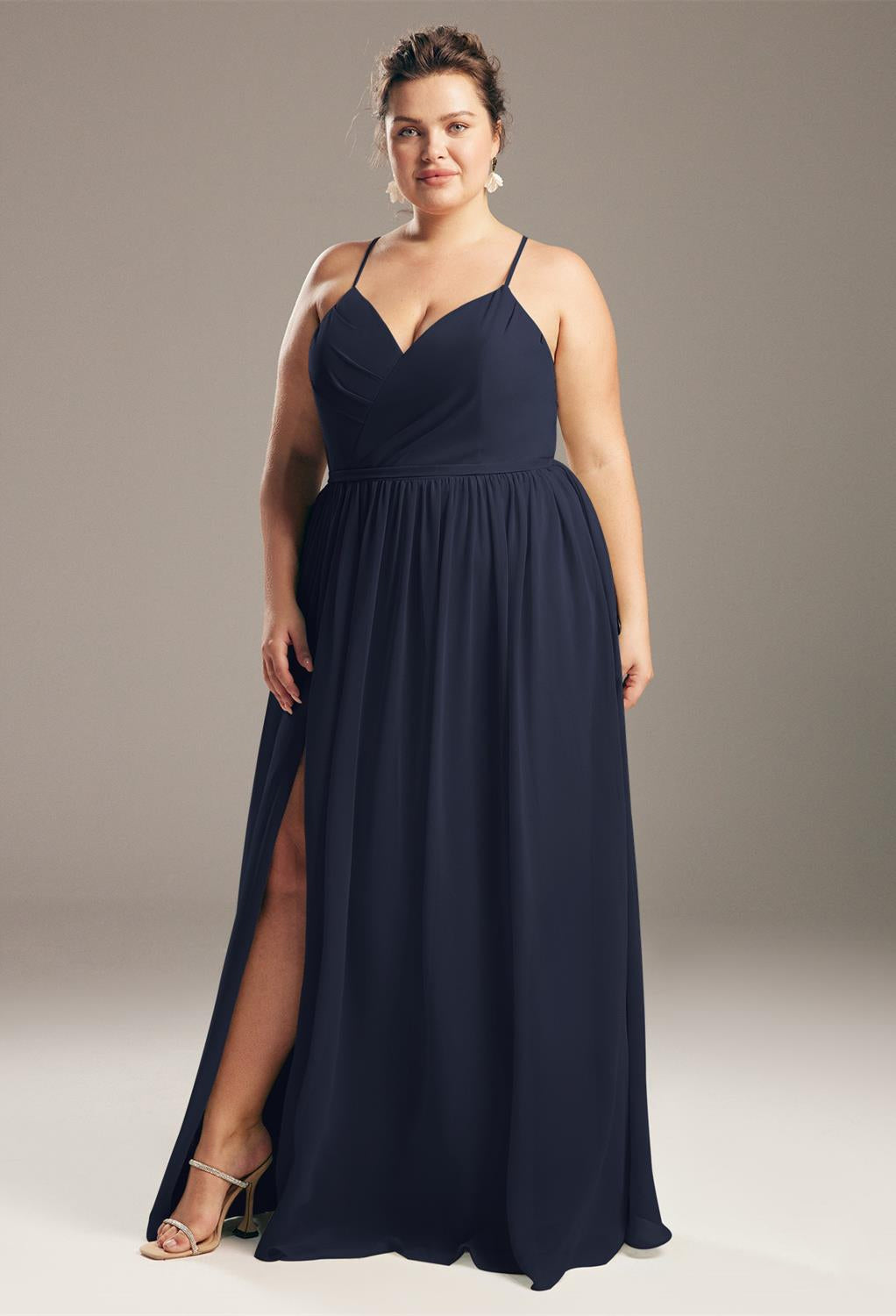 Woman in an elegant Wilfreda - Chiffon Bridesmaid Dress - Off The Rack gown in navy blue with a slit, standing confidently in one of London's Bergamot Bridal shops, looking directly at the camera.