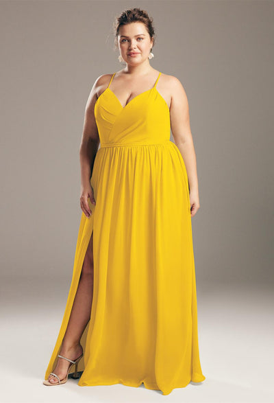 A person wearing a bright yellow chiffon bridesmaid dress with spaghetti straps, reminiscent of the vibrant styles offered by Bergamot Bridal's Wilfreda collection, poses against a gray background in London, Ontario.