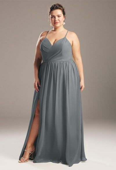 A confident woman in a Wilfreda - Chiffon Bridesmaid Dress from Bergamot Bridal stands against a neutral background, looking directly at the camera.