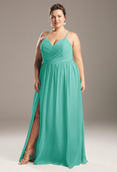 A woman in a flowing mint green dress by Bergamot Bridal with a halter neckline and high slit, standing confidently against a gray background, reminiscent of the elegant styles found in bridal shops.