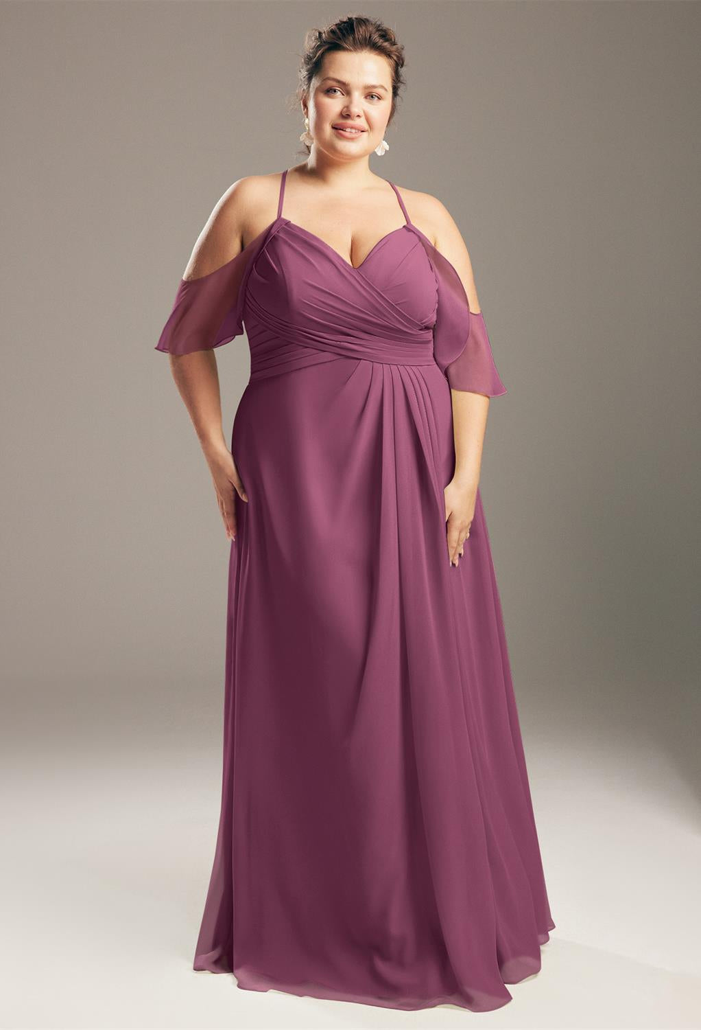 A woman elegantly poses in the Jenifer chiffon bridesmaid dress from Bergamot Bridal, featuring a mauve color with cold-shoulder style, a sweetheart neckline, and a ruched bodice, reminiscent of the stunning bridal attire available at shops in London, Ontario.