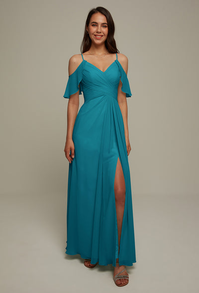 A woman in the Jenifer Chiffon Bridesmaid Dress from Bergamot Bridal stands smiling in an off-the-shoulder teal gown with a thigh-high slit, perfectly capturing the elegance typically found at a bridal shop in London, Ontario.