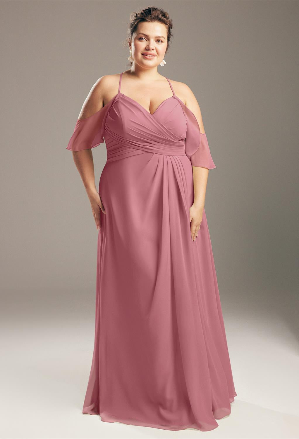 A person stands gracefully in a floor-length Jenifer gown by Bergamot Bridal, featuring off-the-shoulder sleeves and a mauve chiffon fabric that captures the elegance of bridesmaid dresses typically found in London, Ontario.