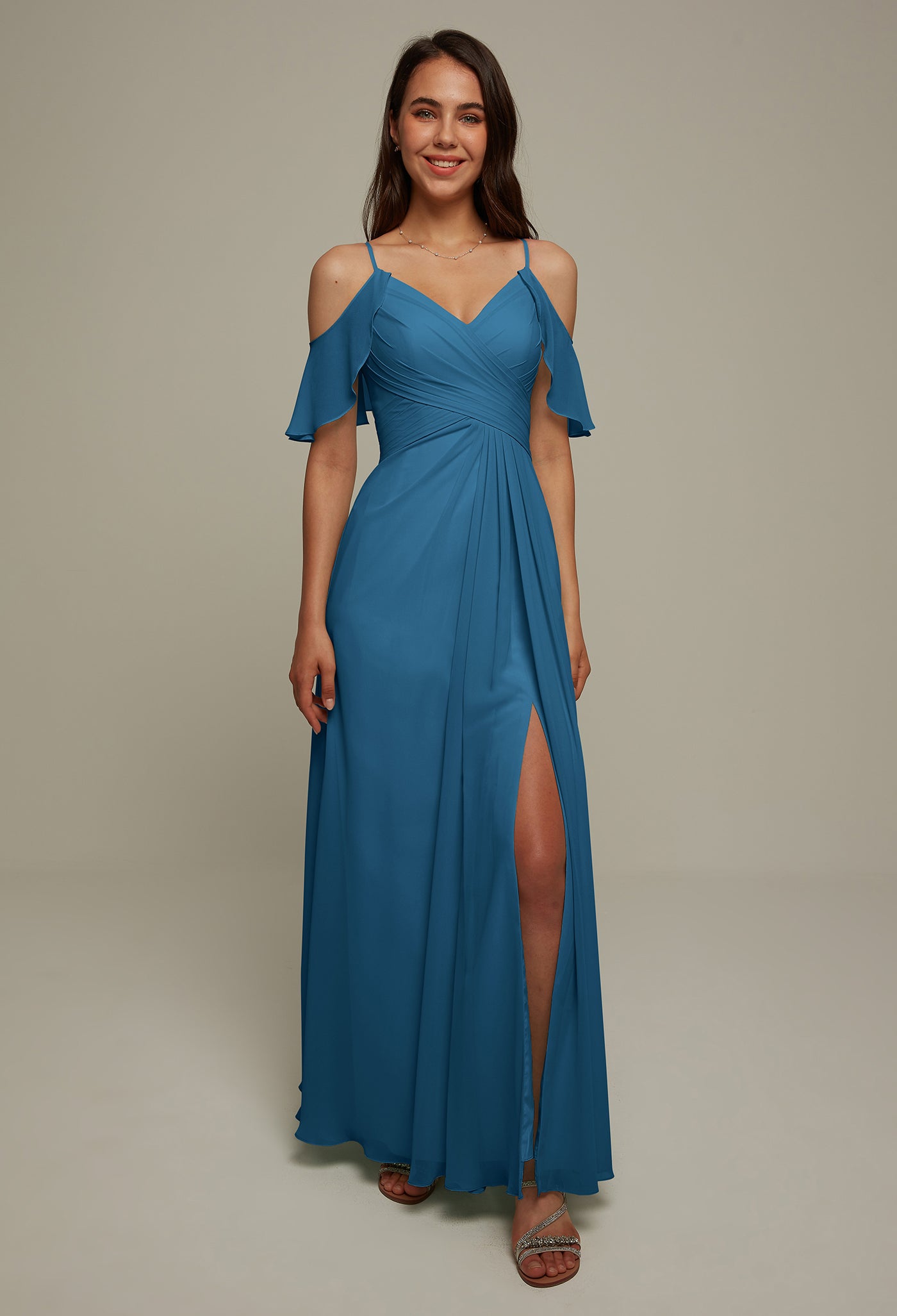 A person wearing the Jenifer chiffon bridesmaid dress from Bergamot Bridal, featuring an off-the-shoulder design and side slit, stands in a neutral background, smiling as if they just stepped out of a bridal shop in London, Ontario.