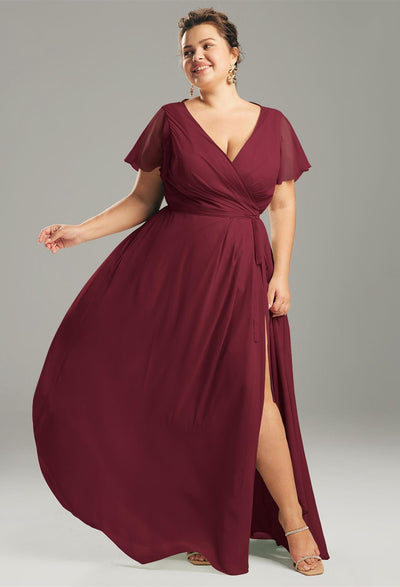 A person wearing the Ellison chiffon wrap dress in a deep red hue, featuring flowing fabric and short sleeves, stands against a plain backdrop, evoking the elegance of off-the-rack bridesmaid dresses from Bergamot Bridal in London, Ontario.