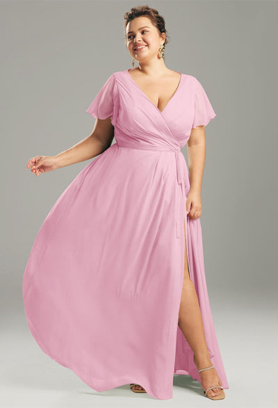 A person wearing Bergamot Bridal's Ellison - Chiffon Bridesmaid Dress in light pink and a pair of sandals poses gracefully against a gray background, evoking the elegant styles found in bridal shops in London, Ontario.