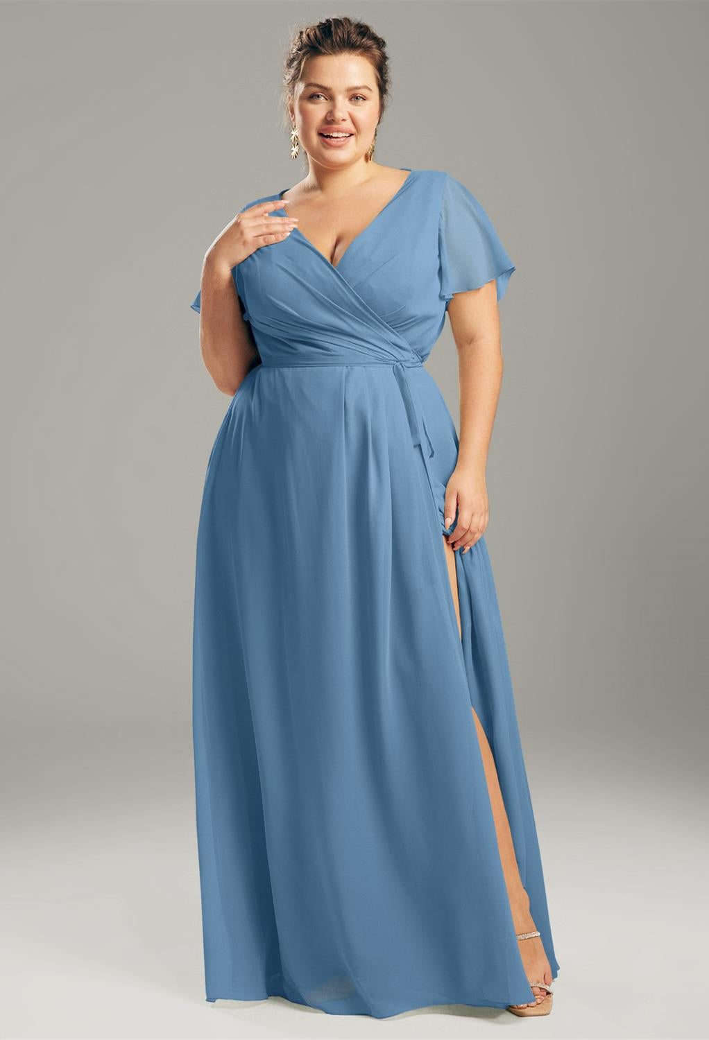 A woman in a blue Ellison - Chiffon Bridesmaid Dress - Off The Rack by Bergamot Bridal with a slit.