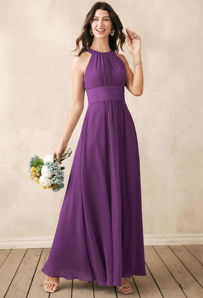 Dressed in the floor-length Dorian Chiffon Bridesmaid Dress, the woman gracefully holds a bouquet against a wooden floor and neutral backdrop. Explore more exquisite bridesmaid dresses from Bergamot Bridal at our shop in London, Ontario.