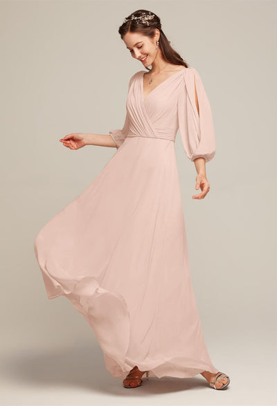 A woman in a flowing Chiffon Bridesmaid Dress named "Polly," designed by Bergamot Bridal, features long sleeves and a V-neckline. She poses with a headband against a neutral background, showcasing the elegance typical of bridal shops in London, Ontario.