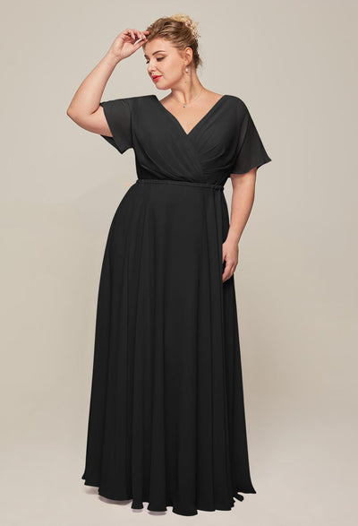 A person in a long, black, wrap-style dress stands against a plain background, touching their hair—exuding timeless elegance reminiscent of the Ginny Chiffon Bridesmaid Dress from Bergamot Bridal, an affordable and sophisticated choice available off the rack in London, Ontario.