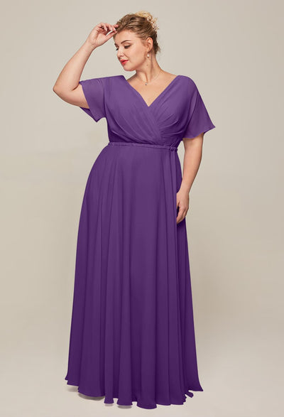 A person in the Ginny chiffon bridesmaid dress by Bergamot Bridal, featuring a deep V-neckline, short sleeves, and a flowing skirt, stands against a neutral background while touching their hair—a stunning option among bridesmaid dresses at an affordable bridal shop in London, Ontario.