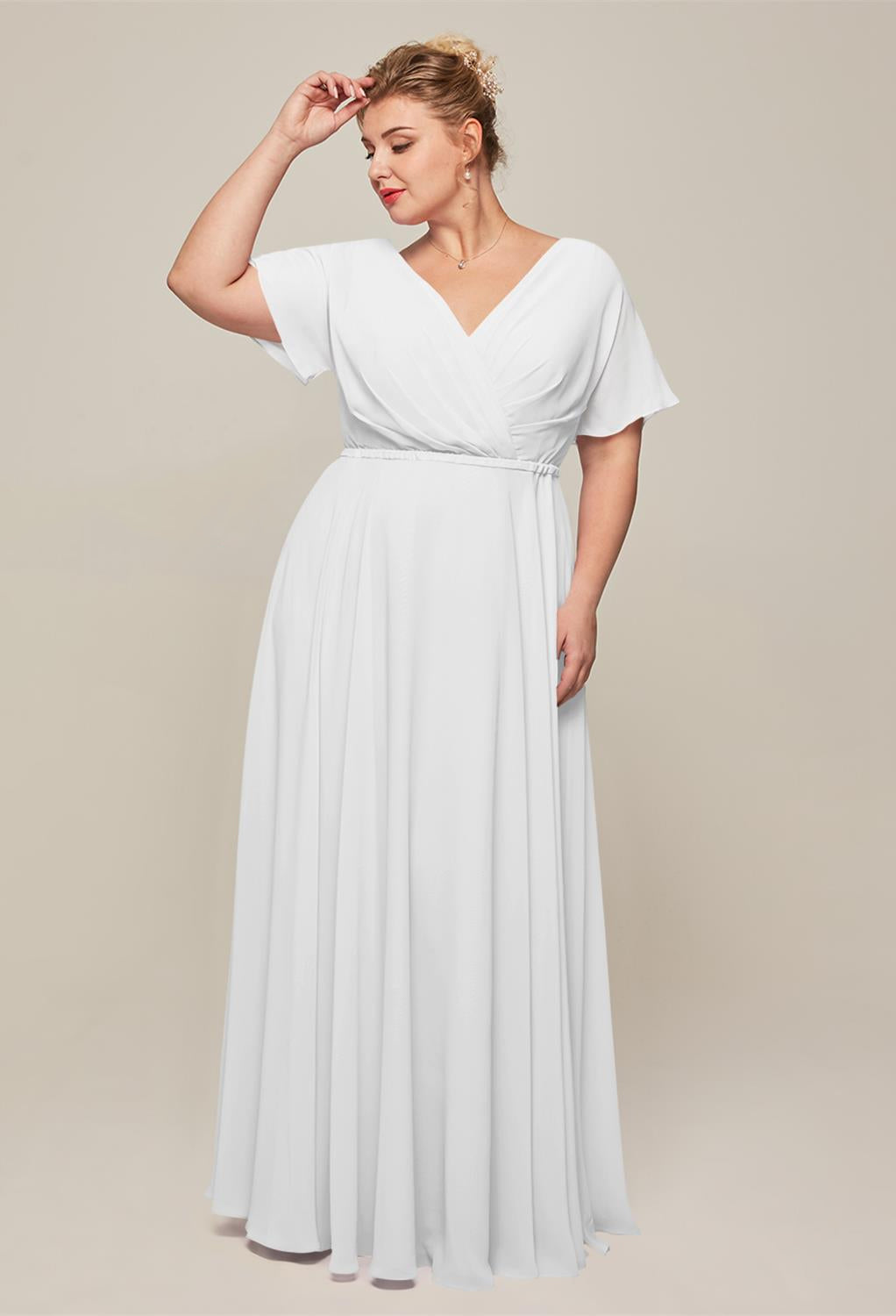 A person in a white gown, reminiscent of the elegant Ginny Chiffon Bridesmaid Dress by Bergamot Bridal, poses with one hand on their head against a plain background.