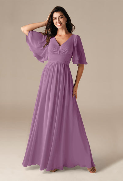 Wearing the Kenney Chiffon Bridesmaid Dress by Bergamot Bridal, a woman poses gracefully against a neutral backdrop, embodying the elegance typical of bridesmaid dresses available off the rack at bridal shops in London, Ontario.