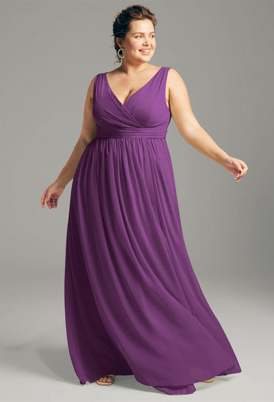 A woman in a sleeveless, purple Bergamot Bridal gown poses against a gray background, exuding the elegance typical of Hilaria chiffon bridesmaid dresses available off the rack in London, Ontario.